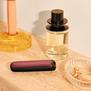 Vaizde matomas Ploom AURA įrenginys su priekiniu dangteliu Dark Orchid, padėtas ant staliuko